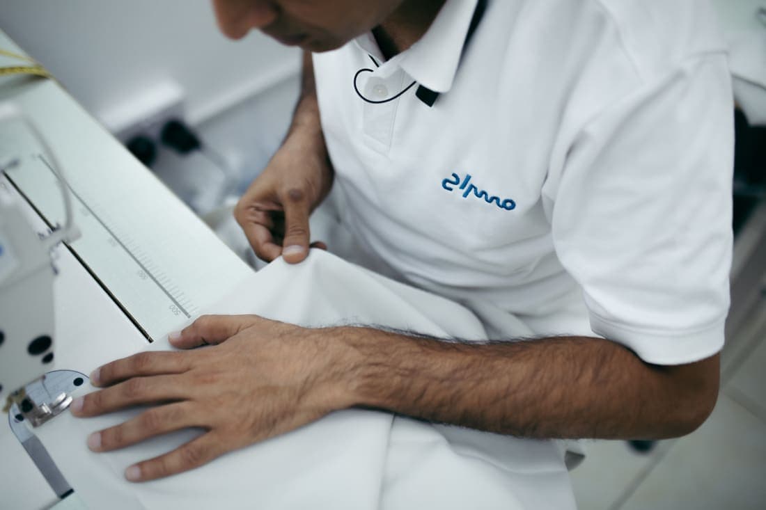 A Misrah tailor guiding white kandura fabric through a sewing machine in the Abu Dhabi workshop.