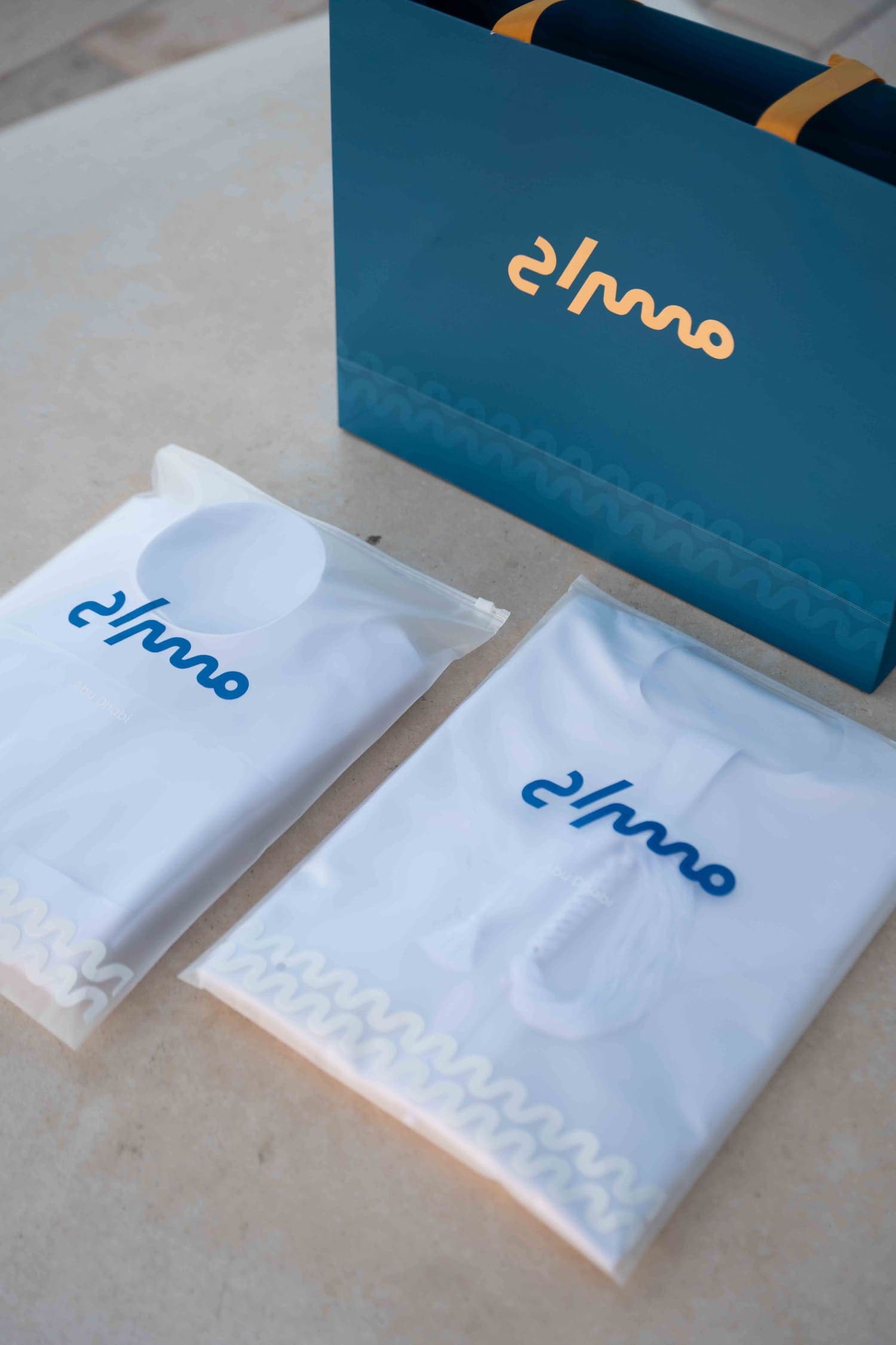 Two folded kanduras in resealable Misrah pouches beside a reusable Misrah bag.