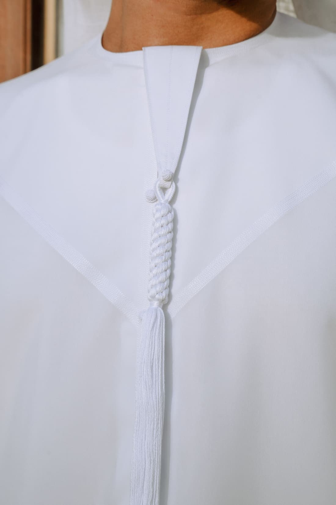 Close view of a white kandura neckline, showing the hand-finished seams and braided tarboosh.